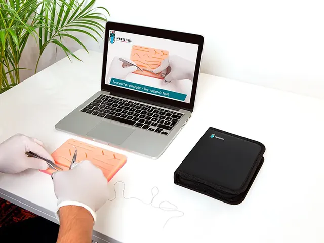 Mains gantées qui s’entraînent à la suture devant un ordinateur portable